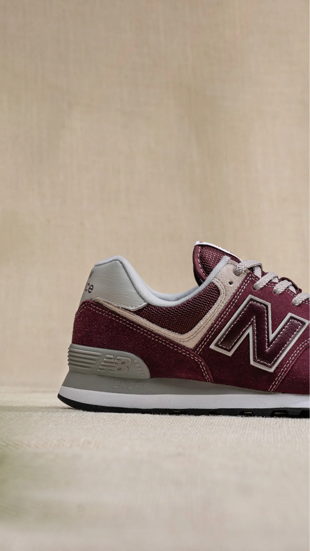 Maroon New Balance sneakers photographed from the side, showing the heel and logo on a beige background on a shoe display shelf